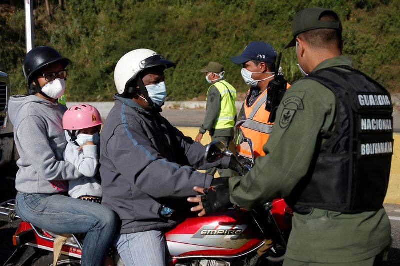 Personas en una motocicleta y usando mascarillas son revisadas por un efectivo de la Guardia Nacional Bolivariana en un punto de control después del inicio de la cuarentena en respuesta a la propagación del coronavirus, en Caracas, Venezuela, Marzo 16, 2020. REUTERS/Manaure Quintero