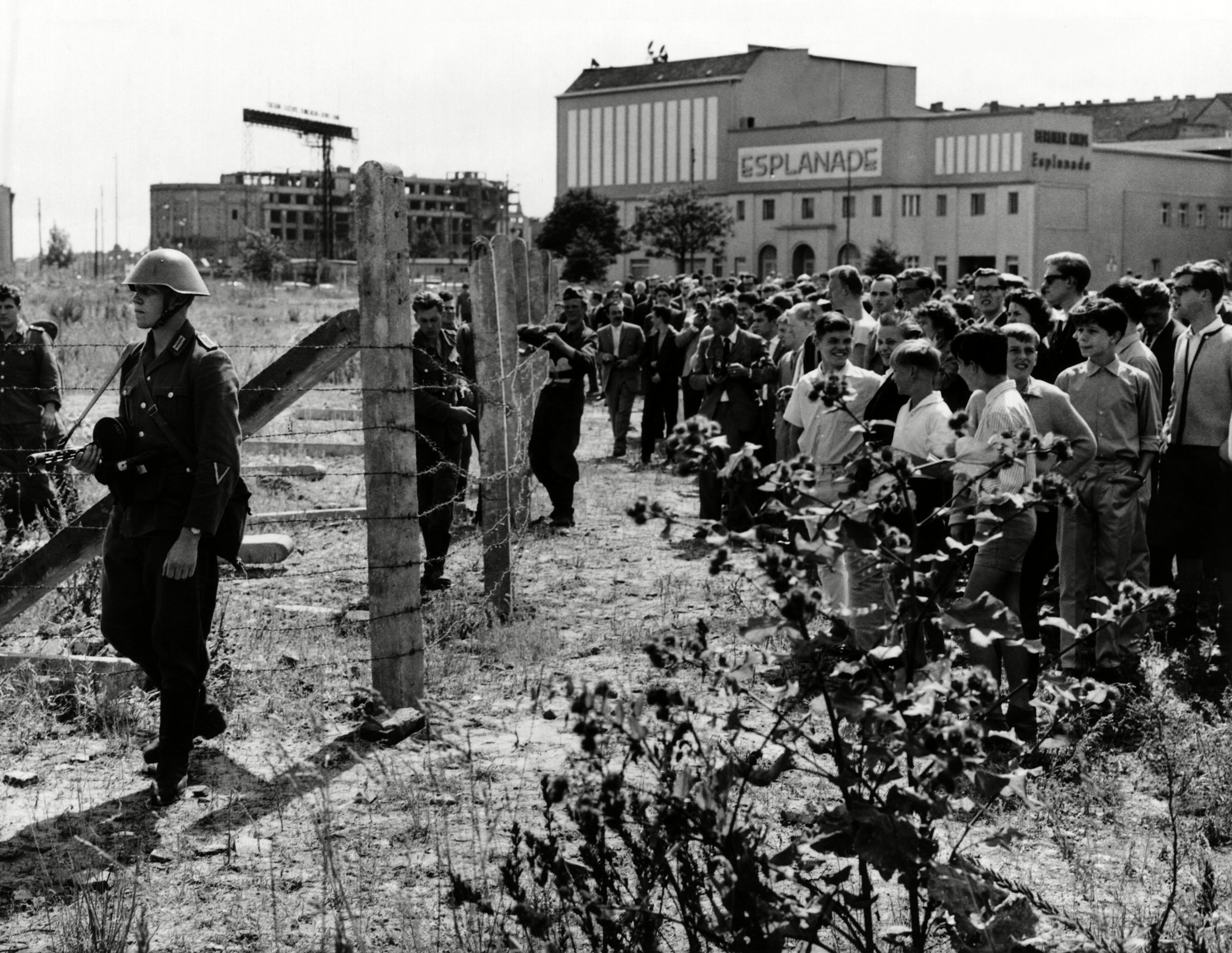 Vecinos de Berlín occidental se juntan frente a los primeros postes y alambres custodiados por guardias orientales el 13 de agosto de 1961.