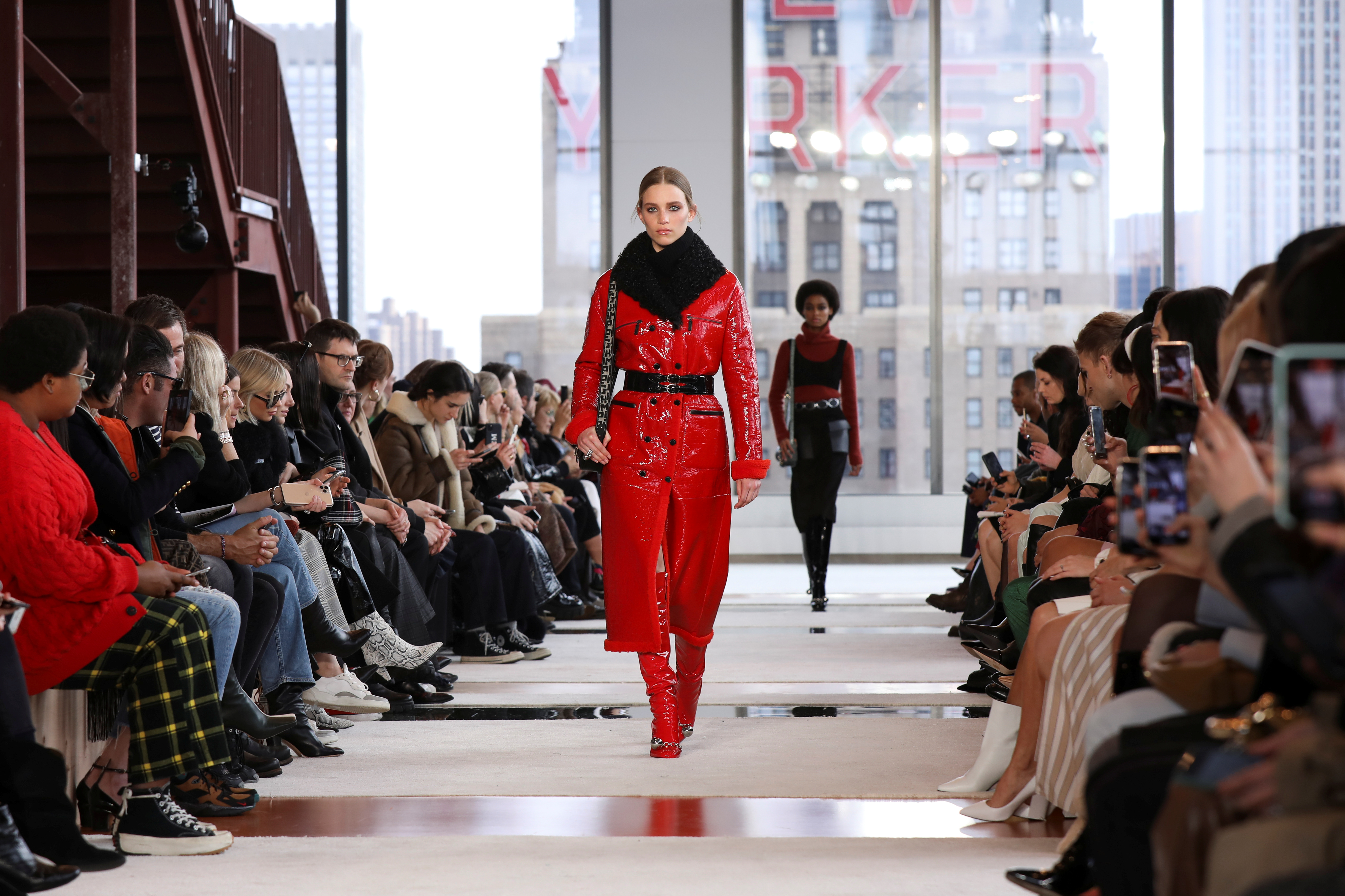 La modelo Rebecca Longendyke desfilando para Longchamp lució un abrigo rojo de vinilo de largo midi, con botas a tono, cinturón de cuero negro y cuello de piel negro. ¿De accesorio? La cartera con correa de logotipo