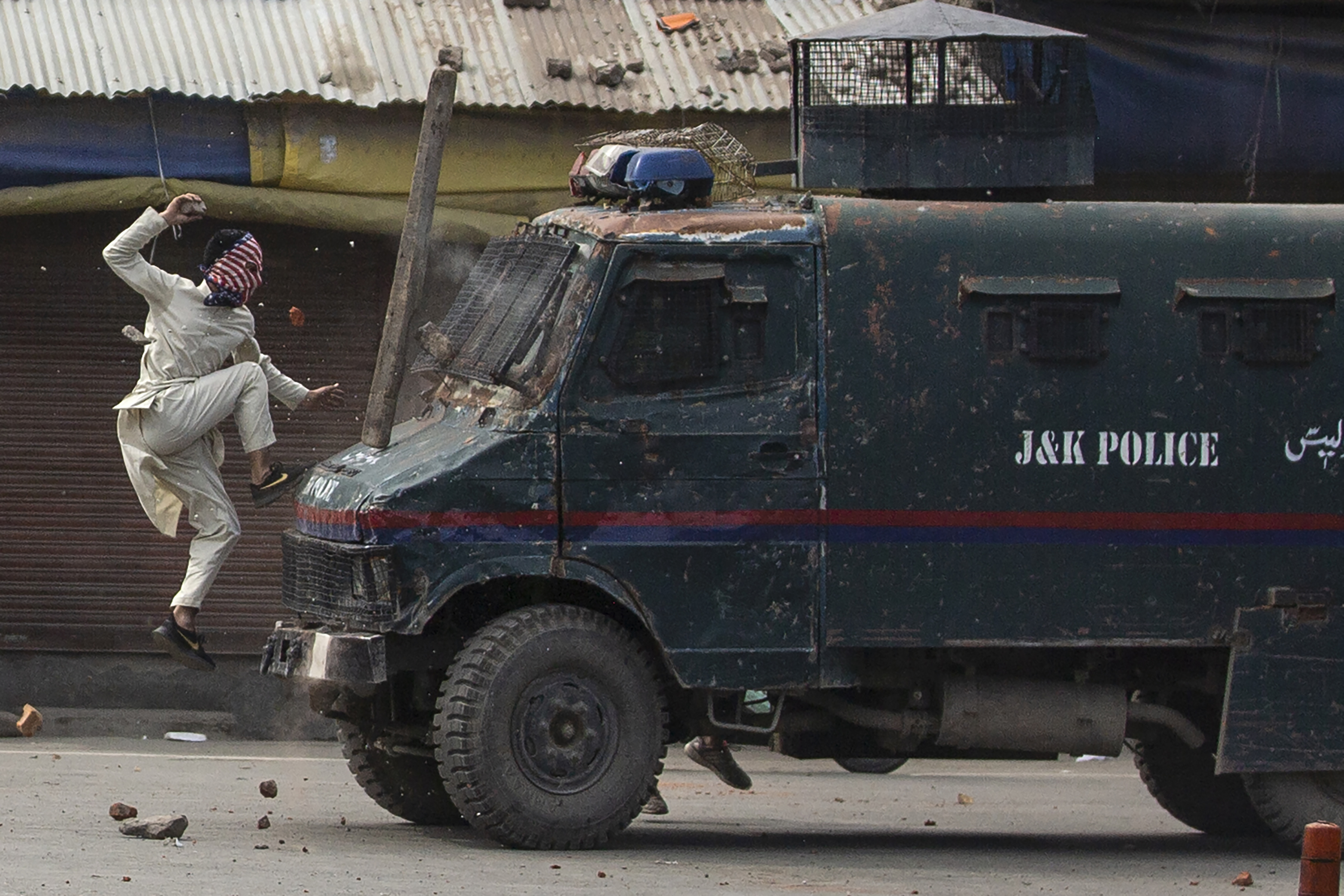 Un manifestante enmascarado de Cachemira salta sobre el capó de un vehículo blindado de la policía india mientras le arroja piedras durante una protesta en Srinagar. (Foto AP / Dar Yasin)