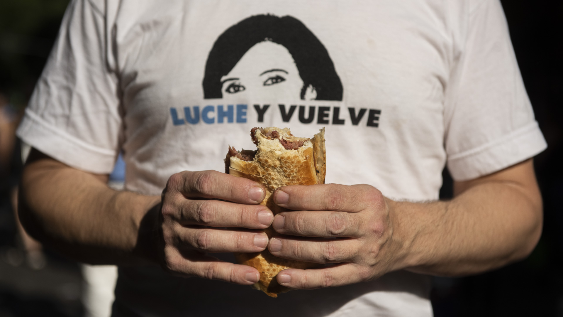 Un militante con una remera de Cristina Kirchner come un choripán junto a sus compañeros