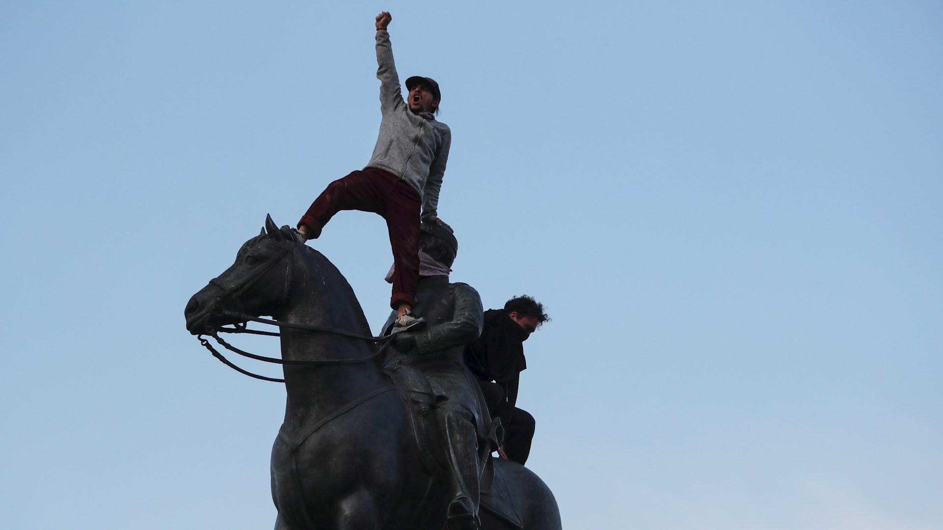 Jóvenes subidos arriba de una estatua en Santiago, Chile