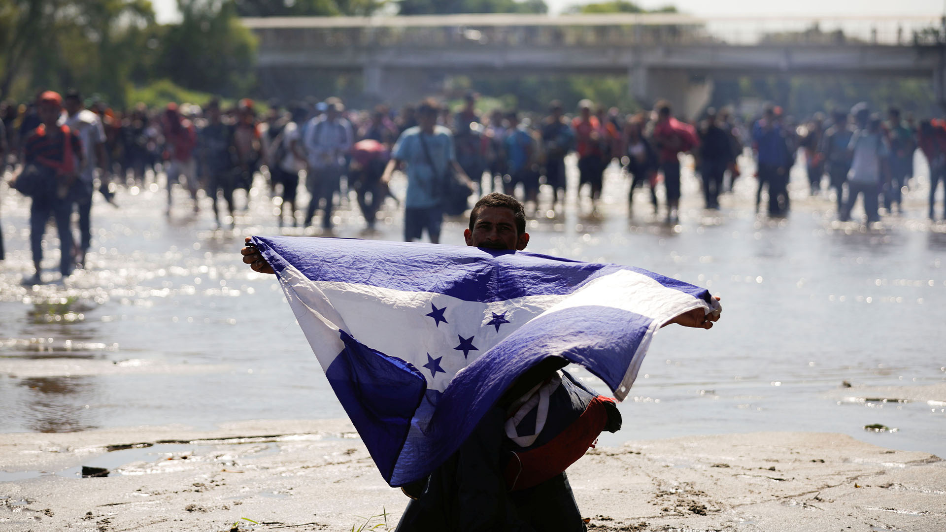 Un inmigrante sostiene la bandera de Honduras mientras intentan cruzar por la fuerza la frontera de México con este país (Foto: José Cabezas/Reuters)