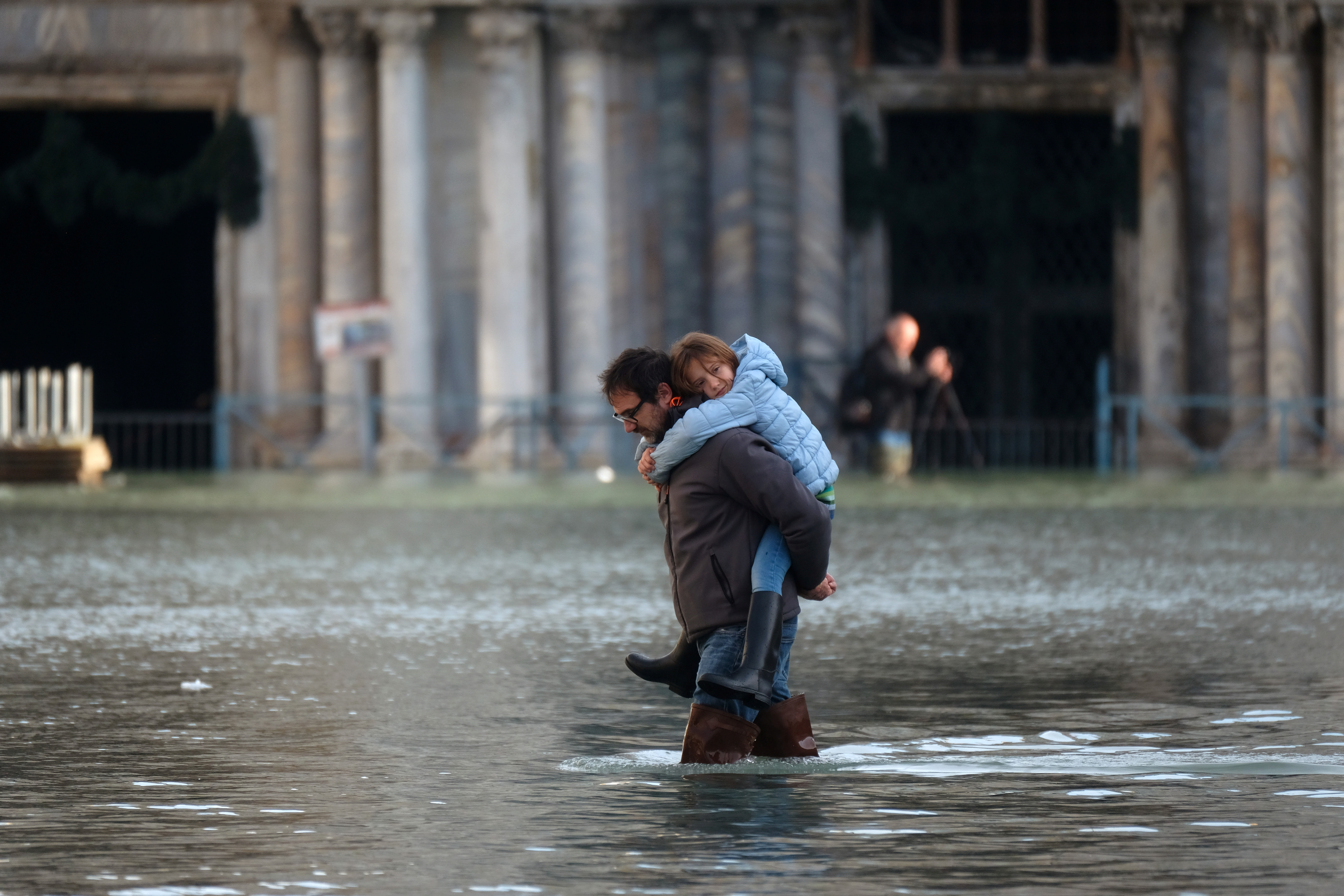 Un hombre carga un niño mientras camina por la inundada Plaza de San Marcos durante la marea alta en Venecia (REUTERS/Manuel Silvestri)