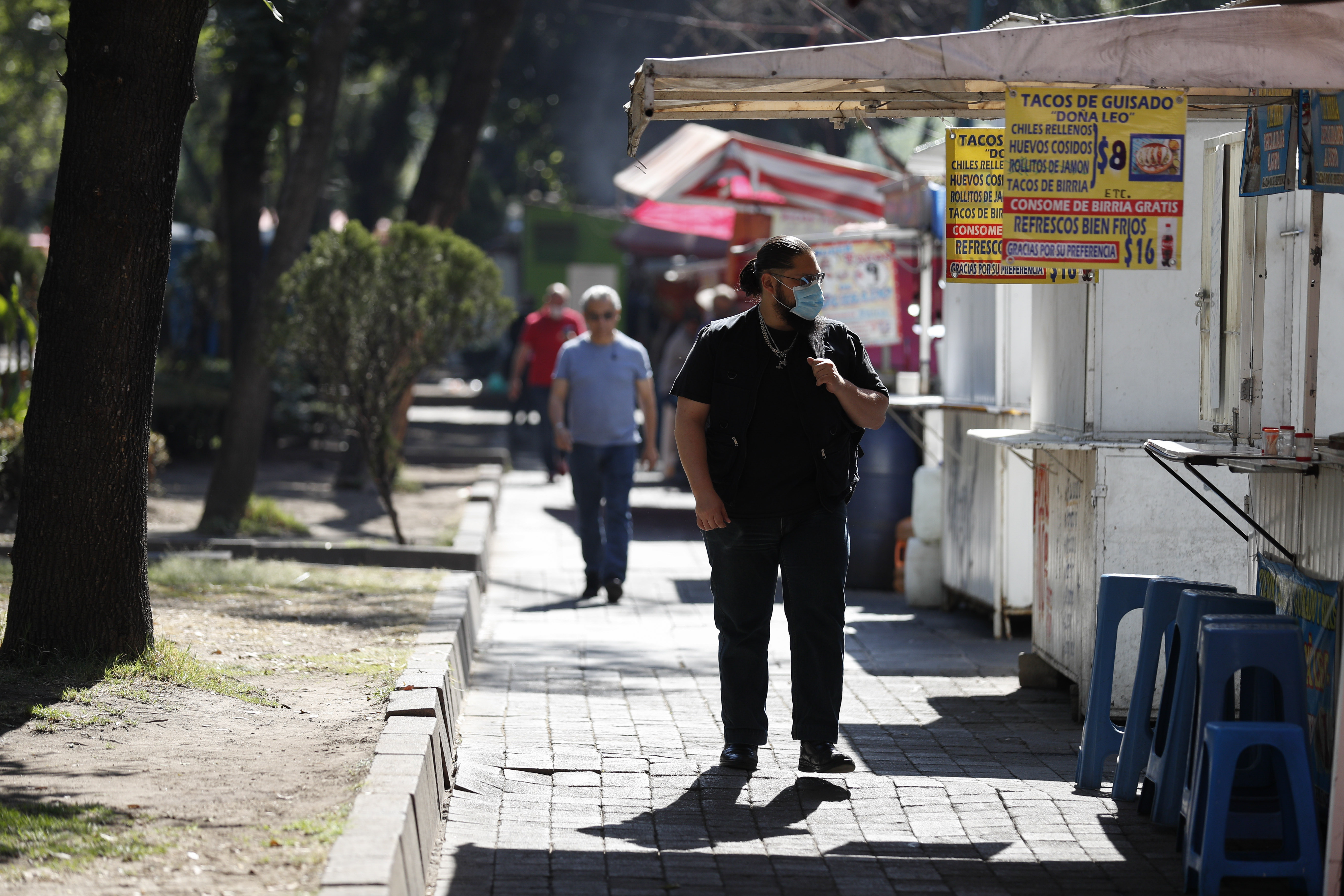 Un hombre con una máscara facial pasa por los puestos callejeros que venden alimentos, la mayoría de los cuales ya estaban abiertos , en la Ciudad de México, el miércoles 25 de marzo de 2020.