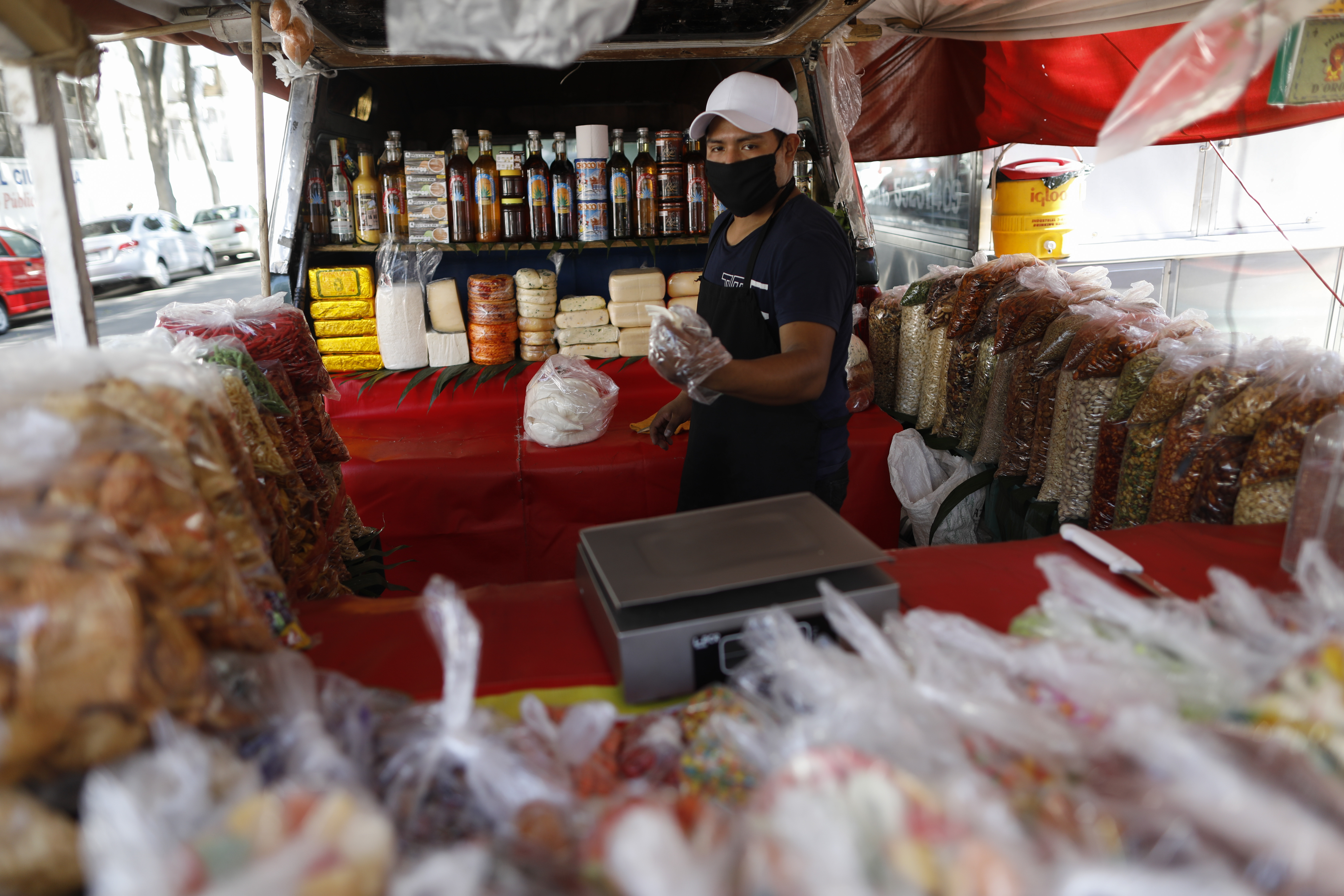 Arturo Torres, de 22 años, con una mascarilla protectora para seguir las nuevas recomendaciones, corta un trozo de queso mientras organiza productos del estado de Oaxaca en un puesto de venta diario detrás de un camión, en la Ciudad de México, el miércoles 25 de marzo de 2020. Torres, quien ha sido empleado de la misma pequeña empresa durante casi cinco años, estima que más de 100 familias viven de la venta de productos oaxaqueños en la parte trasera de los camiones, con empleados que ganan alrededor de 200 pesos por día (alrededor de $ 8.50). Aunque Torres tiene sus dudas sobre los orígenes y la amenaza del nuevo coronavirus, todavía dice que pueden