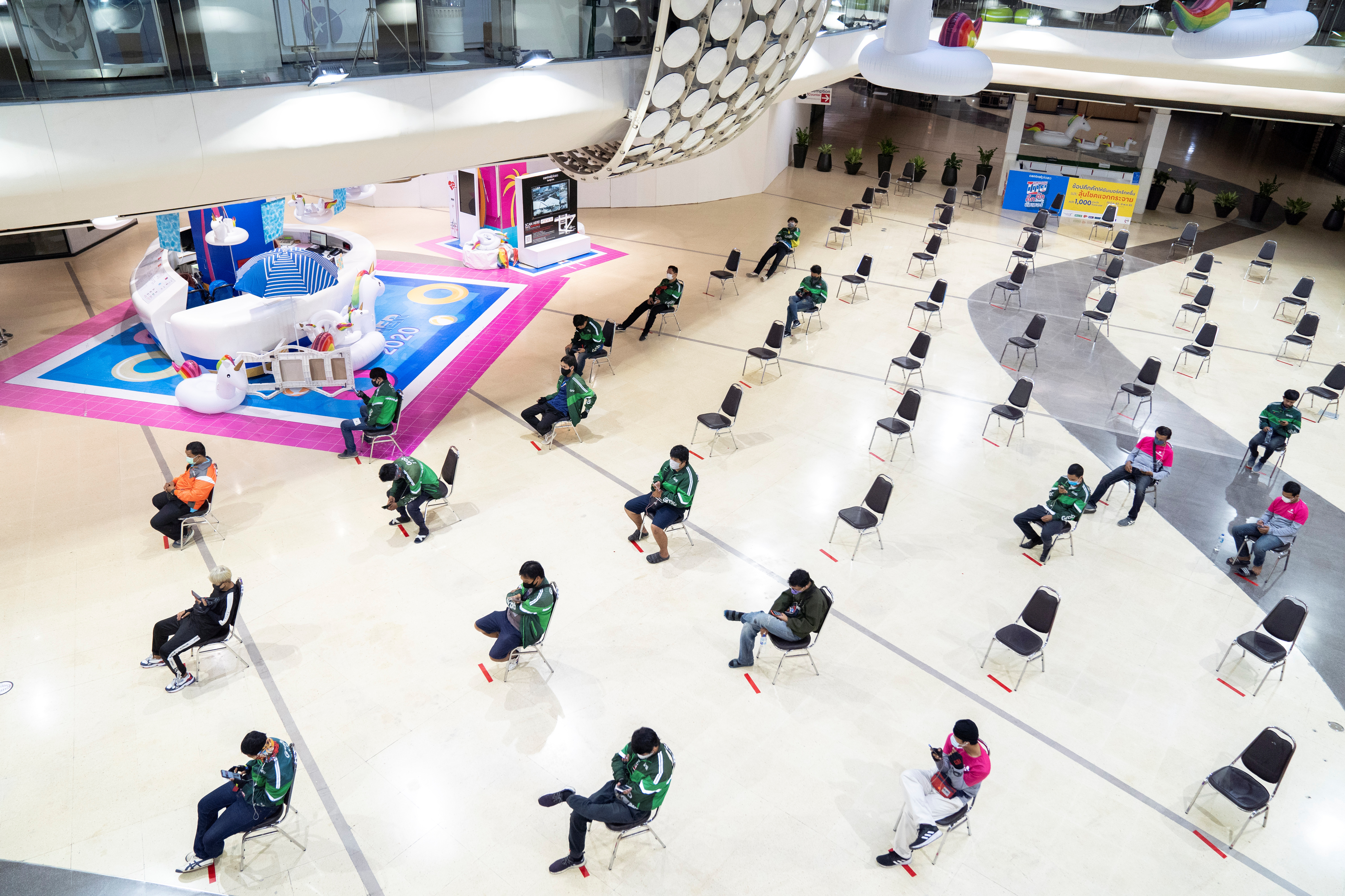 Empleados de delivery esperan pedidos, sentados y manteniendo la distancia social, en un shopping de Bangkok, en Tailandia (REUTERS/Athit Perawongmetha)