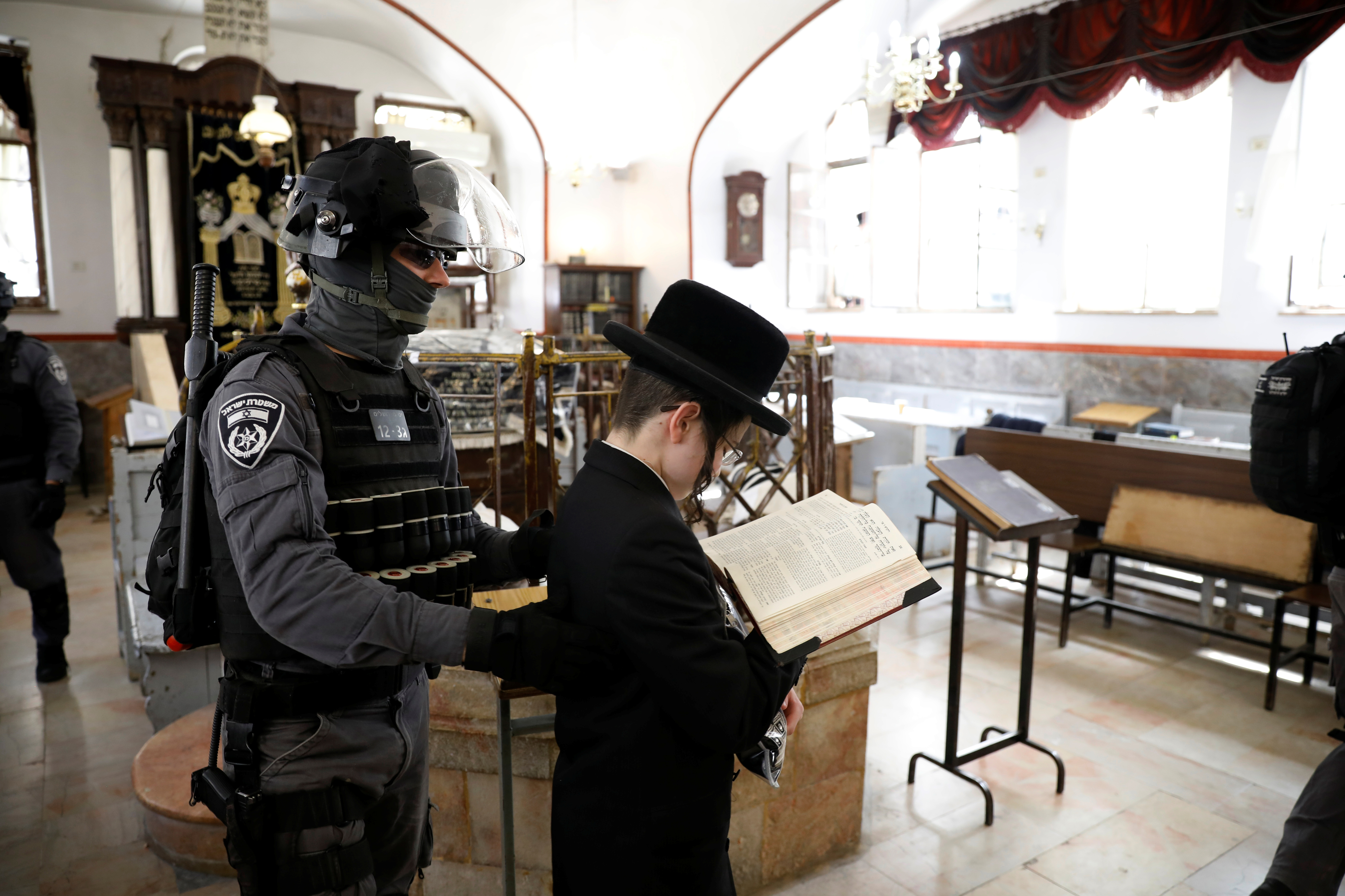 Un policía israelí retira a un joven judío ultraortodoxo de una sinagoga antes de que ésta sea cerrada por la policía, al aplicar las restricciones de un cierre parcial por el COVID-19 en el barrio de Mea Shearim de Jerusalén el 30 de marzo de 2020. (REUTERS/Ronen Zvulun)