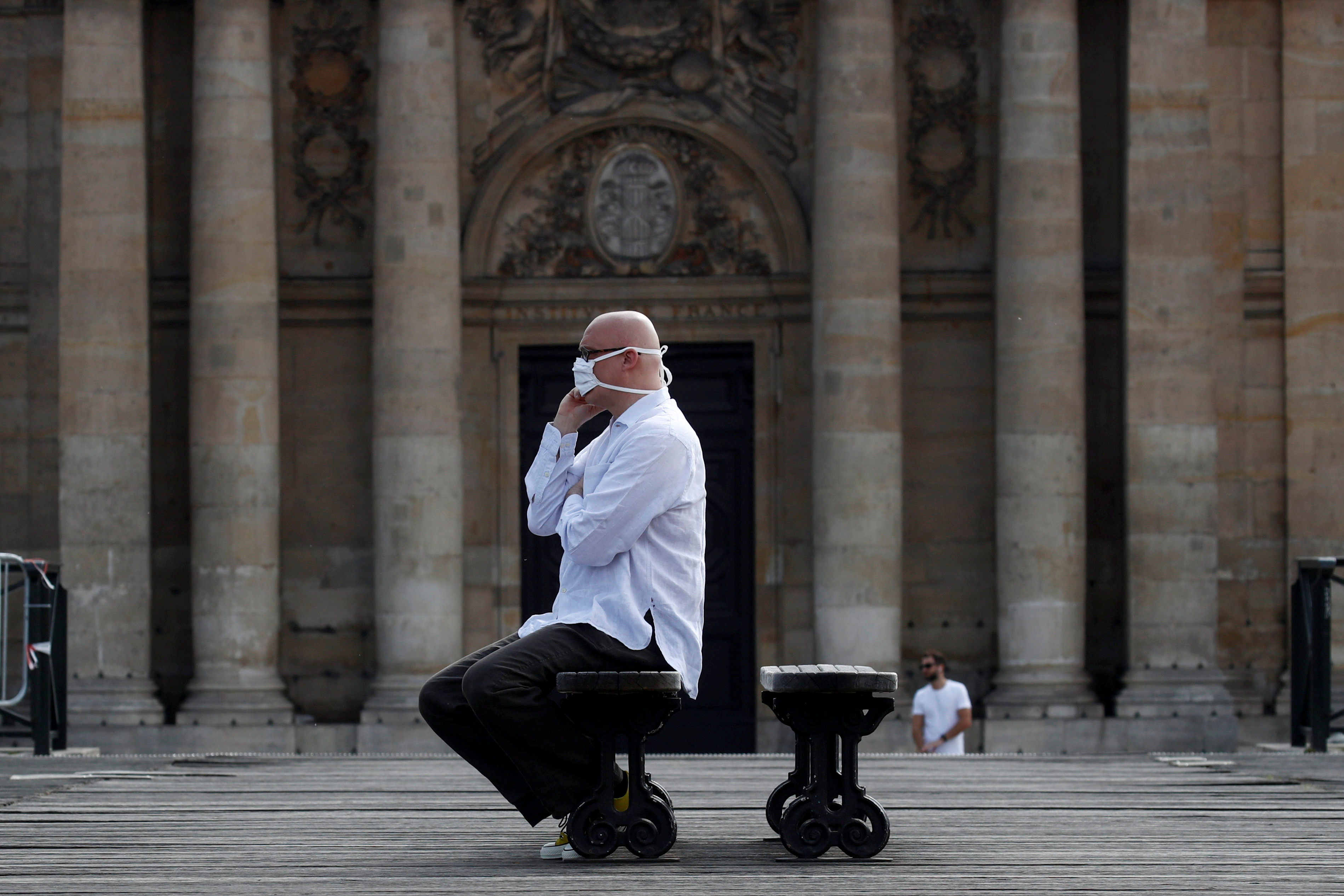 Un hombre con mascarilla reposa en banco del puente de Pont des Arts, en París, durante la pandemia del coronavirus (Reuters)