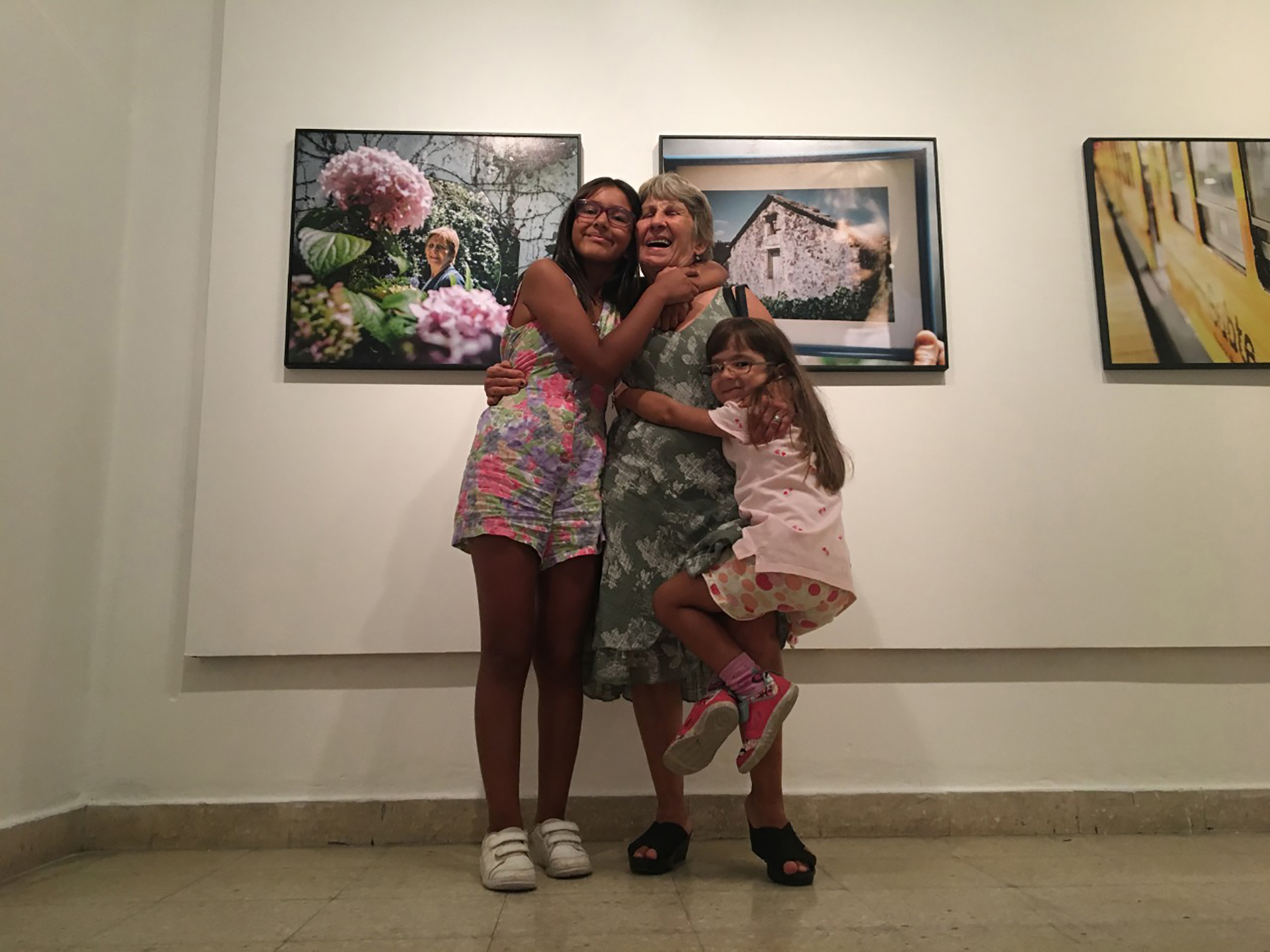 La autora de "Aurlia quiere oír" junto a sus nietas. Detrás la foto de su casa de la infancia en Galicia. (María Rosa Iglesias)
