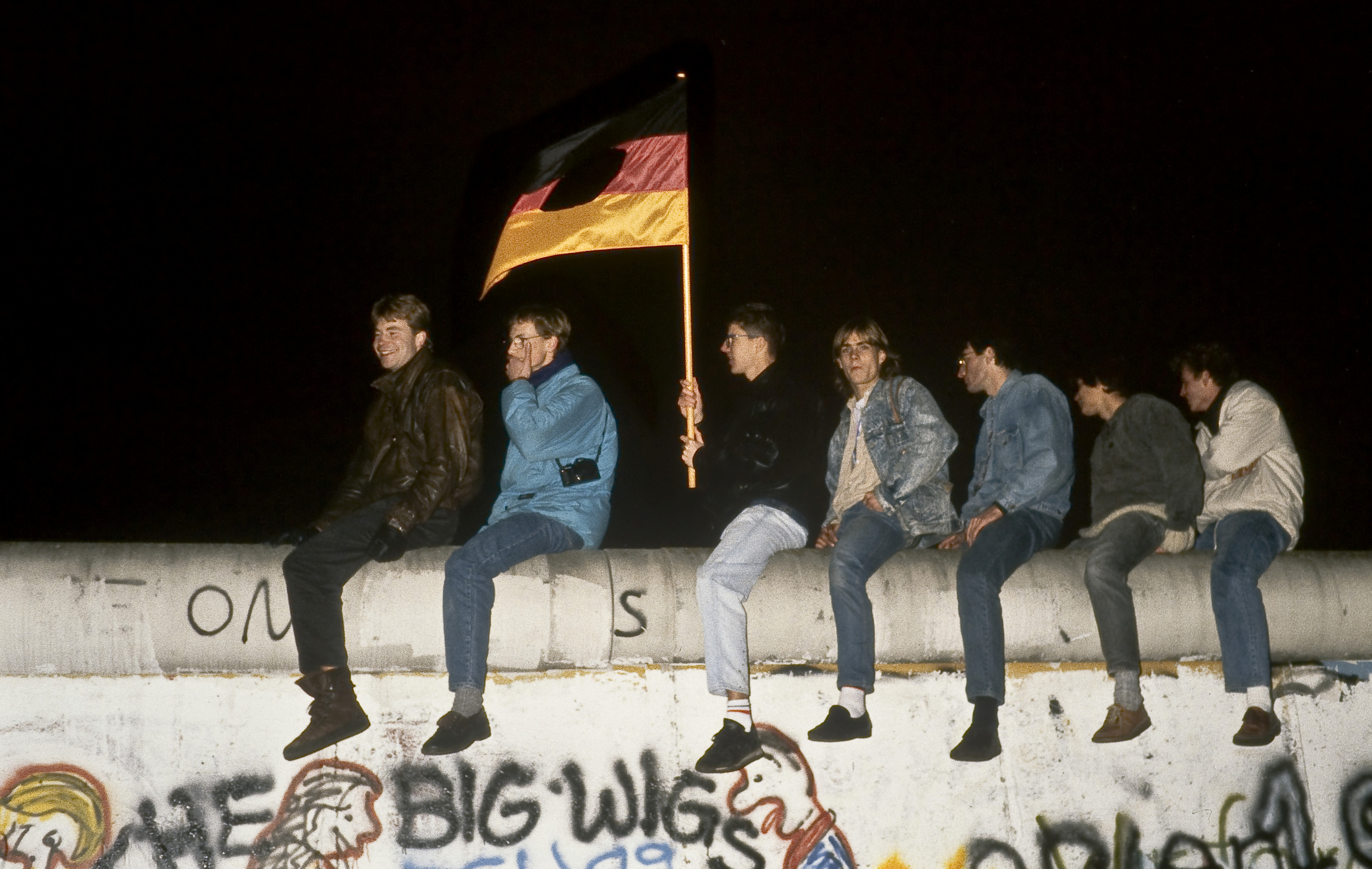 Un joven con la bandera de la Alemania Oriental con su escudo central recortado, sobre el muro, la noche del 9 de noviembre.