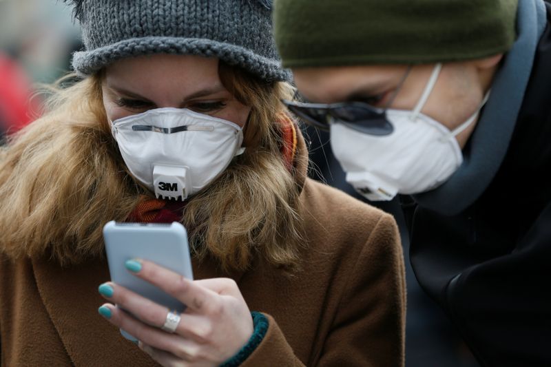 Personas utilizando mascarillas mientras usan sus teléfonos inteligentes en una calle durante el brote de COVID-19, la enfermedad que causa el coronavirus, en Kiev, Ucrania (REUTERS/Valentyn Ogirenko)