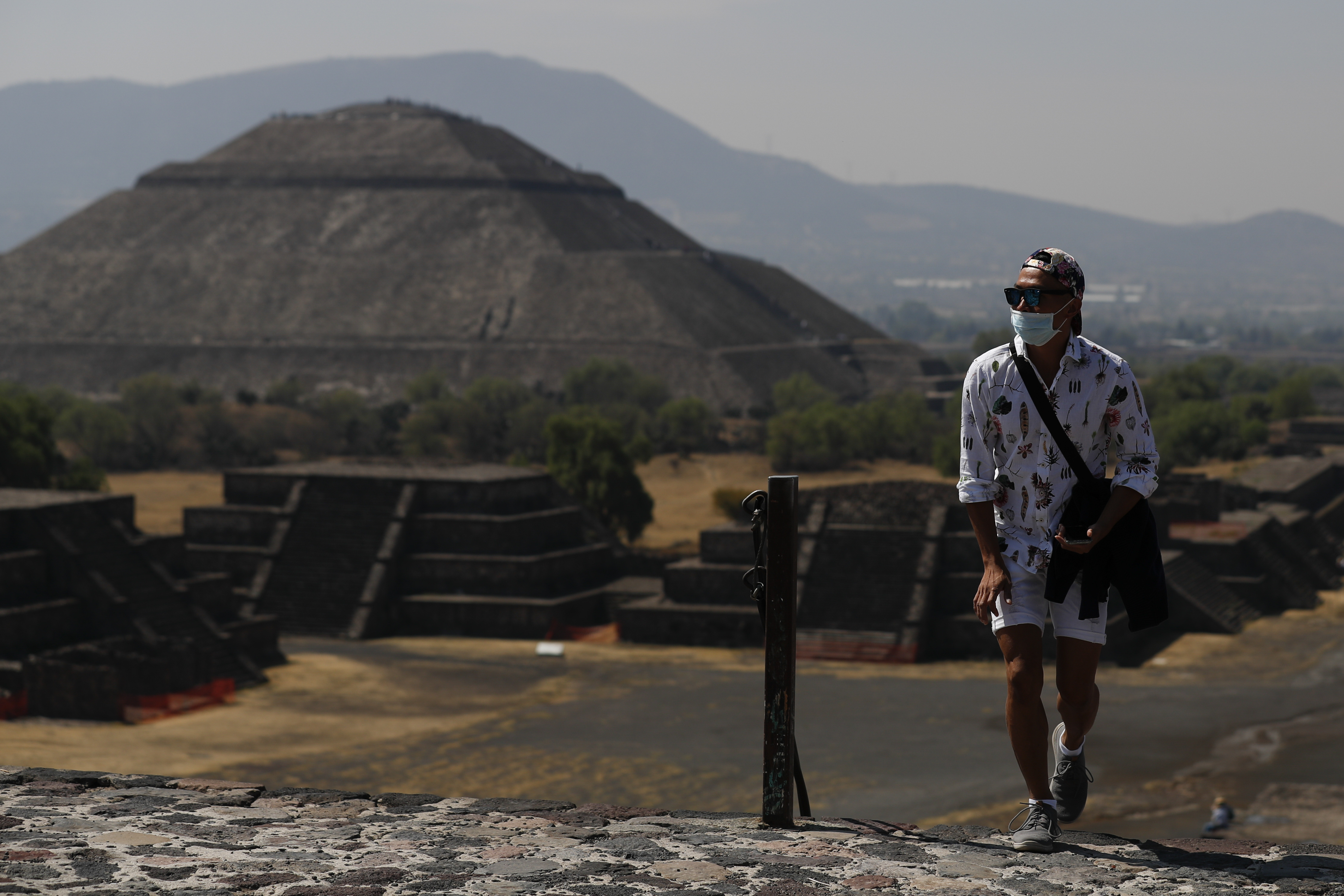 Un visitante con una máscara facial protectora sube la Pirámide de la Luna, con la Pirámide del Sol vista de fondo, en Teotihuacan, México, el jueves 19 de marzo de 2020.