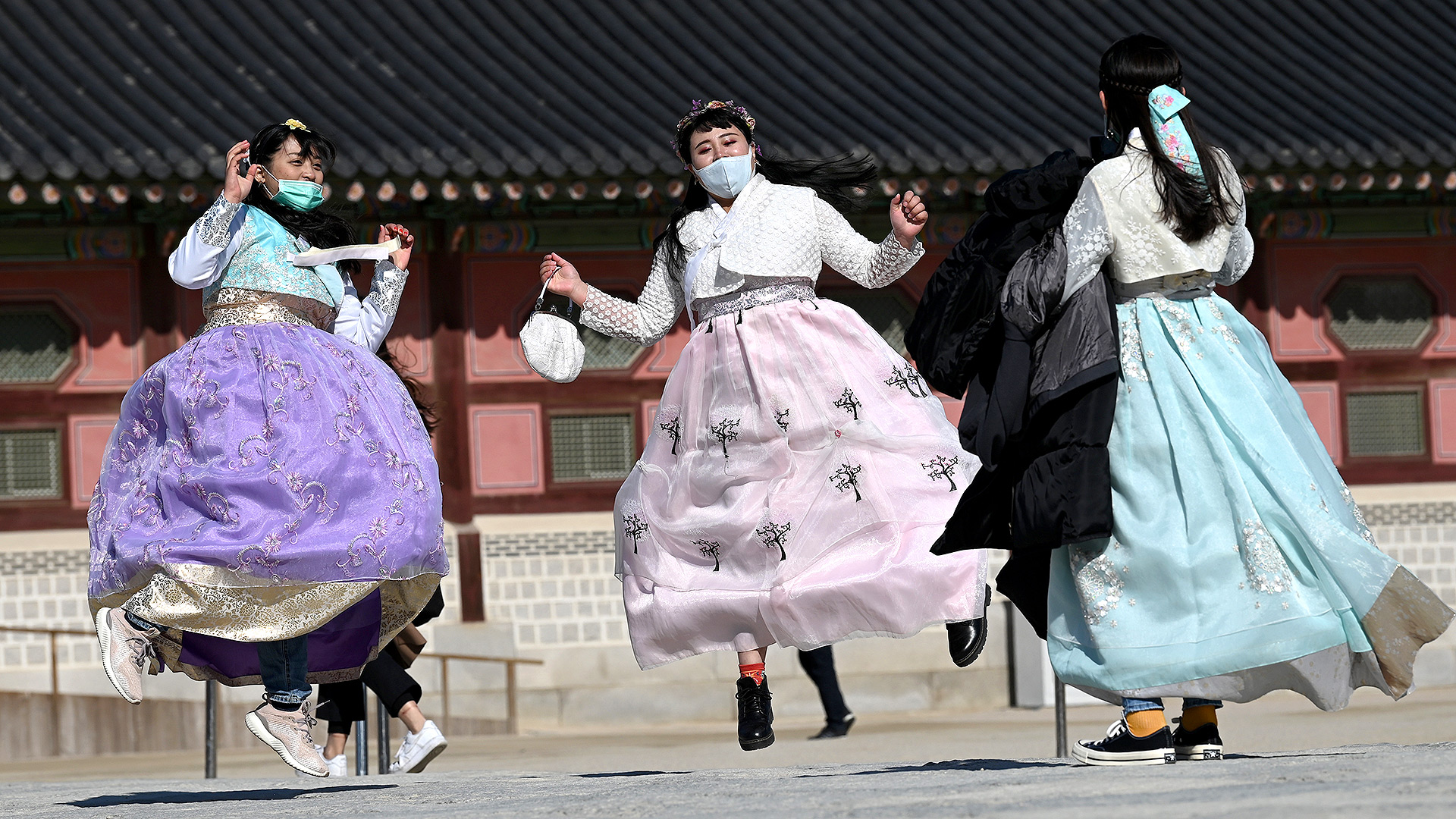 Las personas con vestidos tradicionales de hanbok coreanos usan máscaras faciales mientras saltan para una foto de recuerdo en el palacio Gyeongbokgung en Seúl el 3 de febrero de 2020 (Jung Yeon-je / AFP)
