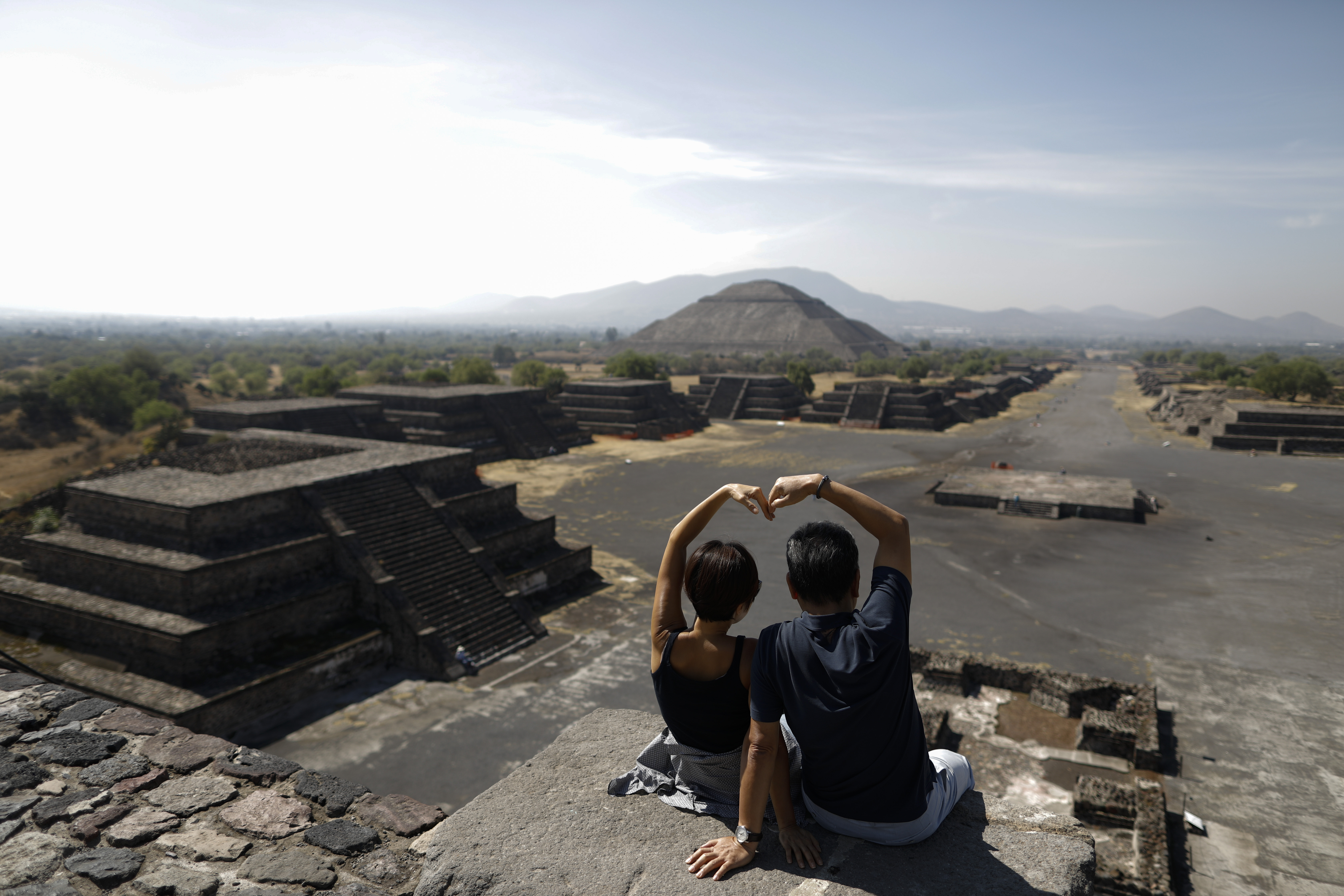 Los turistas surcoreanos Myung Hee Lee, a la izquierda, y Byung Ho Im, forman un corazón con sus manos mientras posan para fotos en la cima de la Pirámide de la Luna, en Teotihuacan, México, el jueves 19 de marzo de 2020. La pareja aprovechó luego de quedar atrapados en la Ciudad de México para visitar las pirámides, después de que su vuelo a casa de unas vacaciones en Cancún y Cuba fuera cancelado.