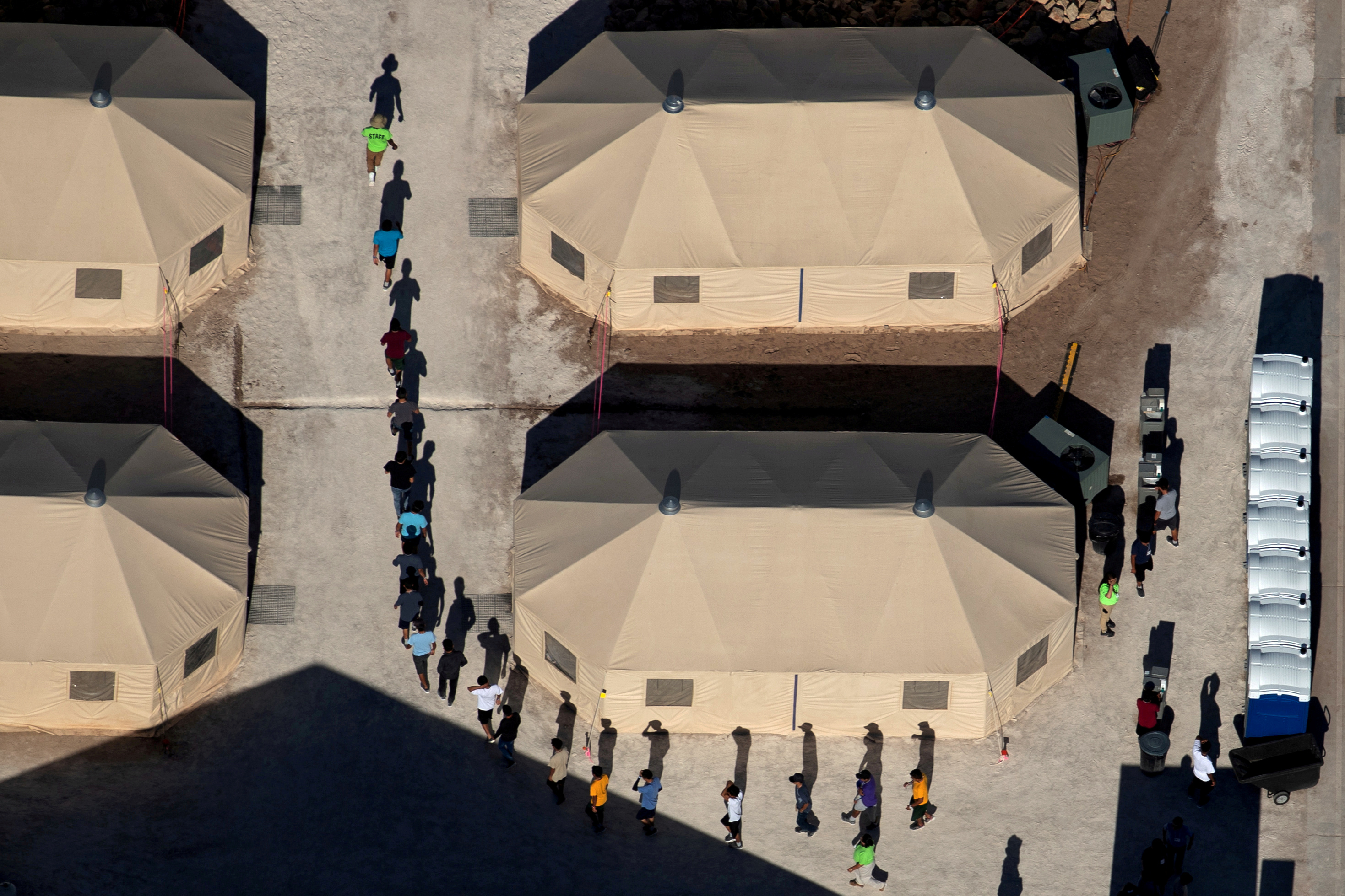 Niños inmigrantes son guiados en fila entre tiendas de campaña en un centro de detención cerca de la frontera con México en Tornillo, Texas, el 18 de junio de 2018 (REUTERS/Mike Blake)