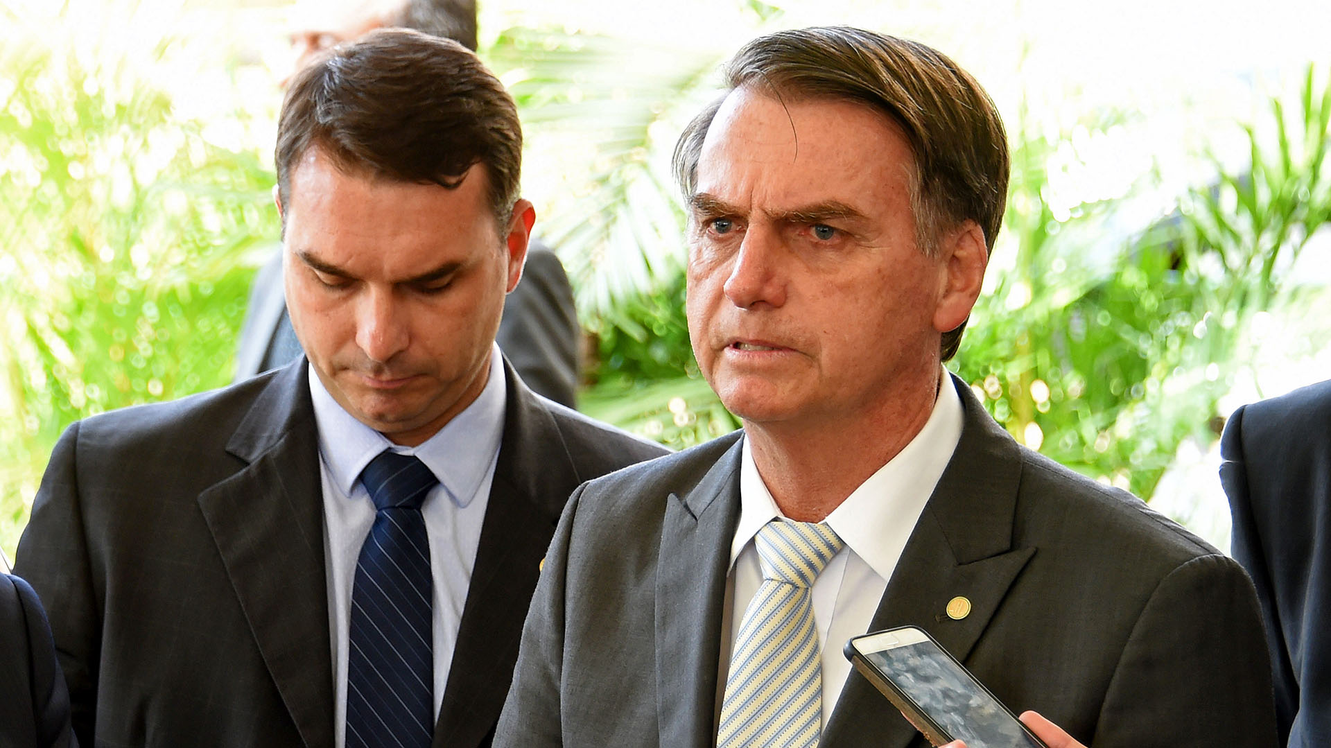 El presidente electo de Brasil, Jair Bolsonaro (R), junto a su hijo y senador Flavio Bolsonaro, y su designado Ministro de Infraestructura, Tarcisio Gomes de Freitas (L), se prepara para hablar ante la prensa en la sede del gobierno de transición en Brasilia, el 27 de noviembre de 2018. (Foto por EVARISTO SA / AFP)