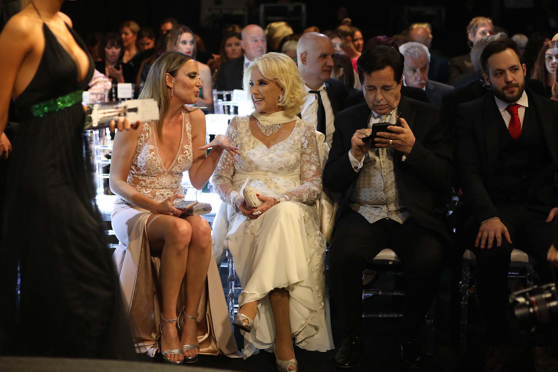 Mirtha -espléndida en nude con un vestido de los hermanos Iara- se ríe junto a Soledad Villarreal -en un Cosano con tajo y transparencias- que se acercó especialmente para hablar con la diva. La dueña de los almuerzos contó: “Yo me pruebo la ropa un día a la semana, con Vidal Rivas elegimos los modelos, cada vez que tengo más años soy más coqueta, quiero que sepan que esta fiesta es maravillosa y que sería bueno que apoyen un poco a la industria textil, que está pasando momentos muy delicados. Este Gobierno, o el que venga, que ayuden a la industria textil. Muchas gracias, esta noche va a ser inolvidable”