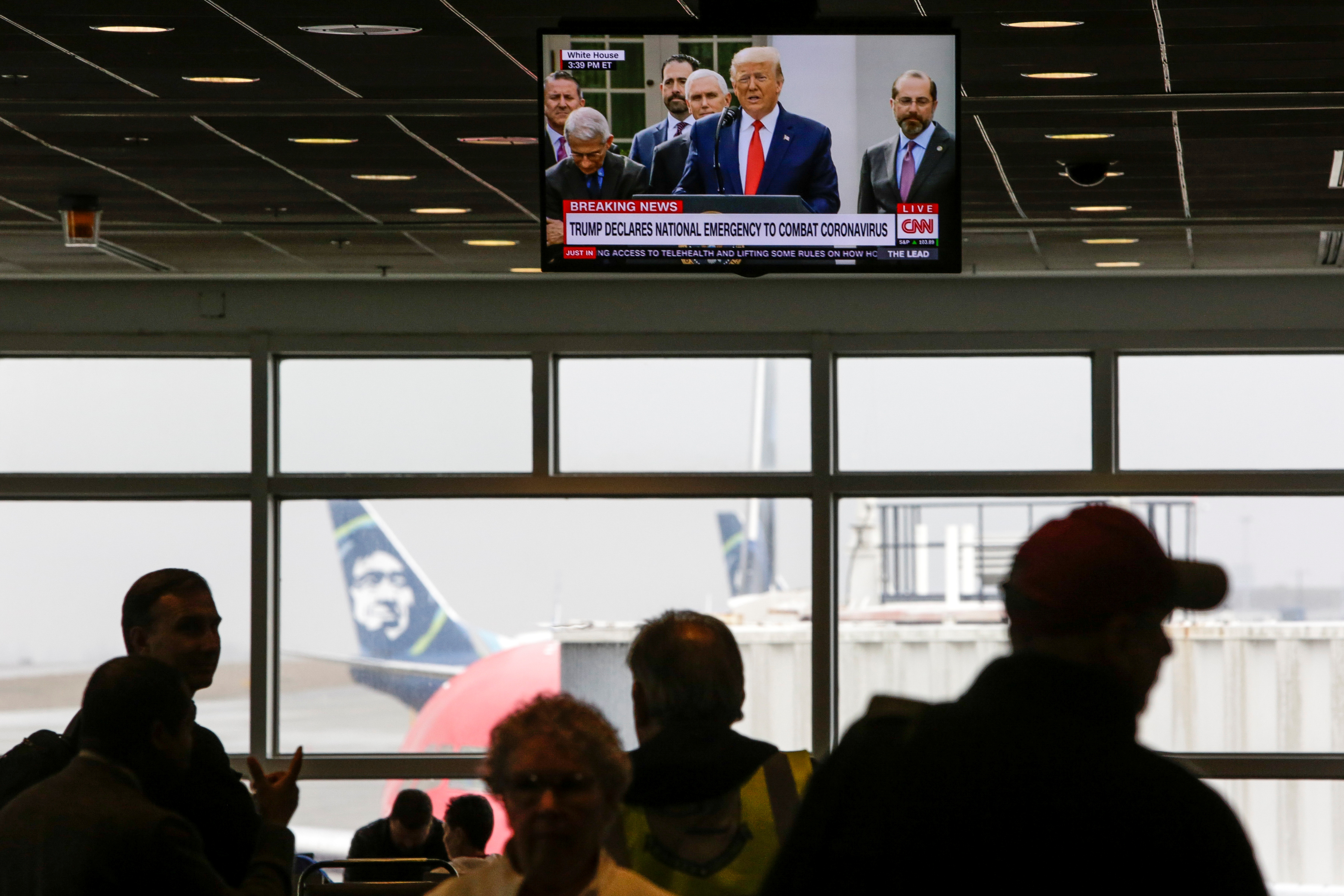 Viajeros ven como el Presidente de los Estados Unidos Donald Trump en un televisor en el Aeropuerto Internacional de Seattle-Tacoma mientras declara una emergencia nacional por el coronavirus, en SeaTac Washington, EE.UU. 13 de marzo de 2020.