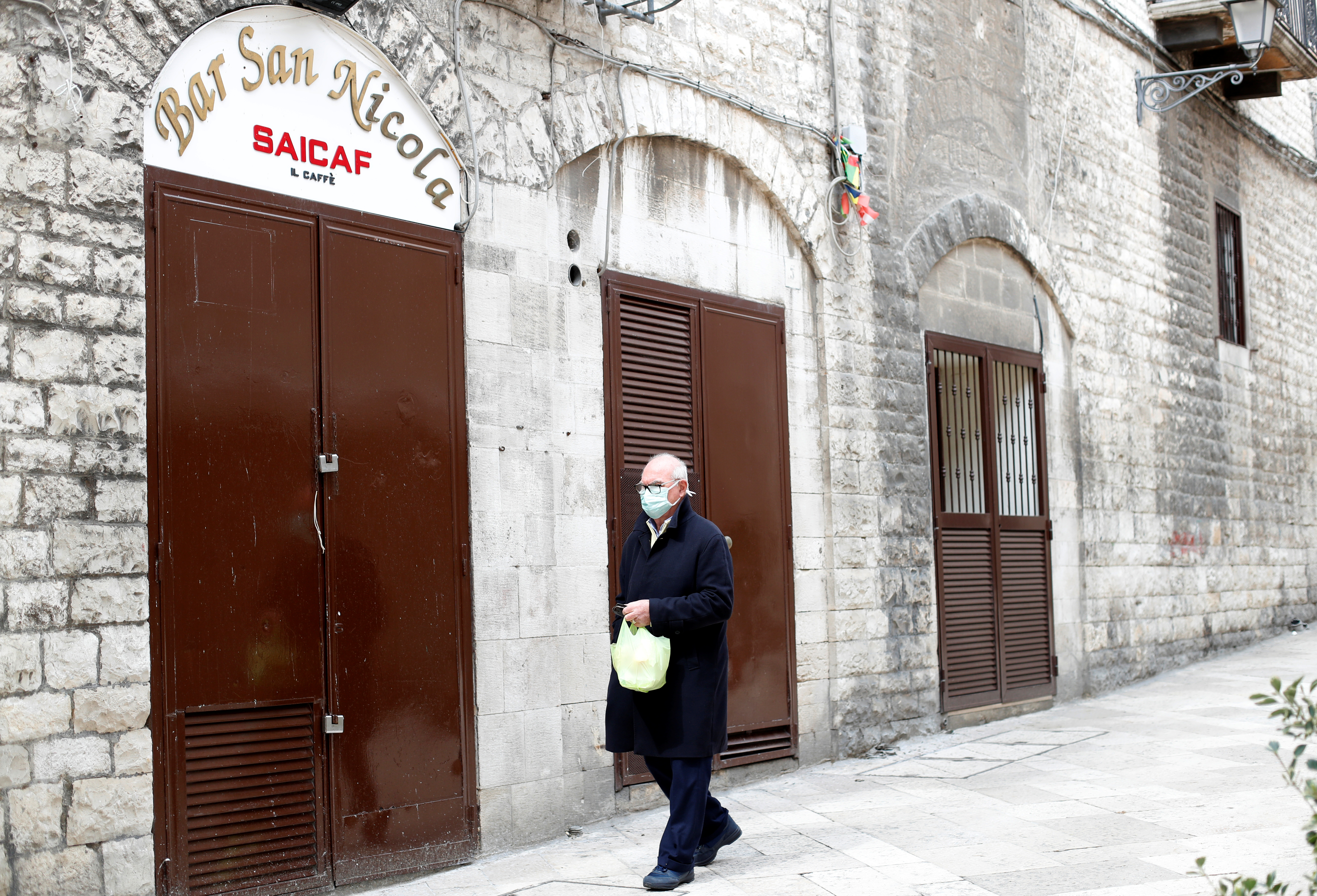 Un hombre mayor con su barbijo camina frente a un bar cerado en Bari, Italia. (REUTERS/Alessandro Garofalo)