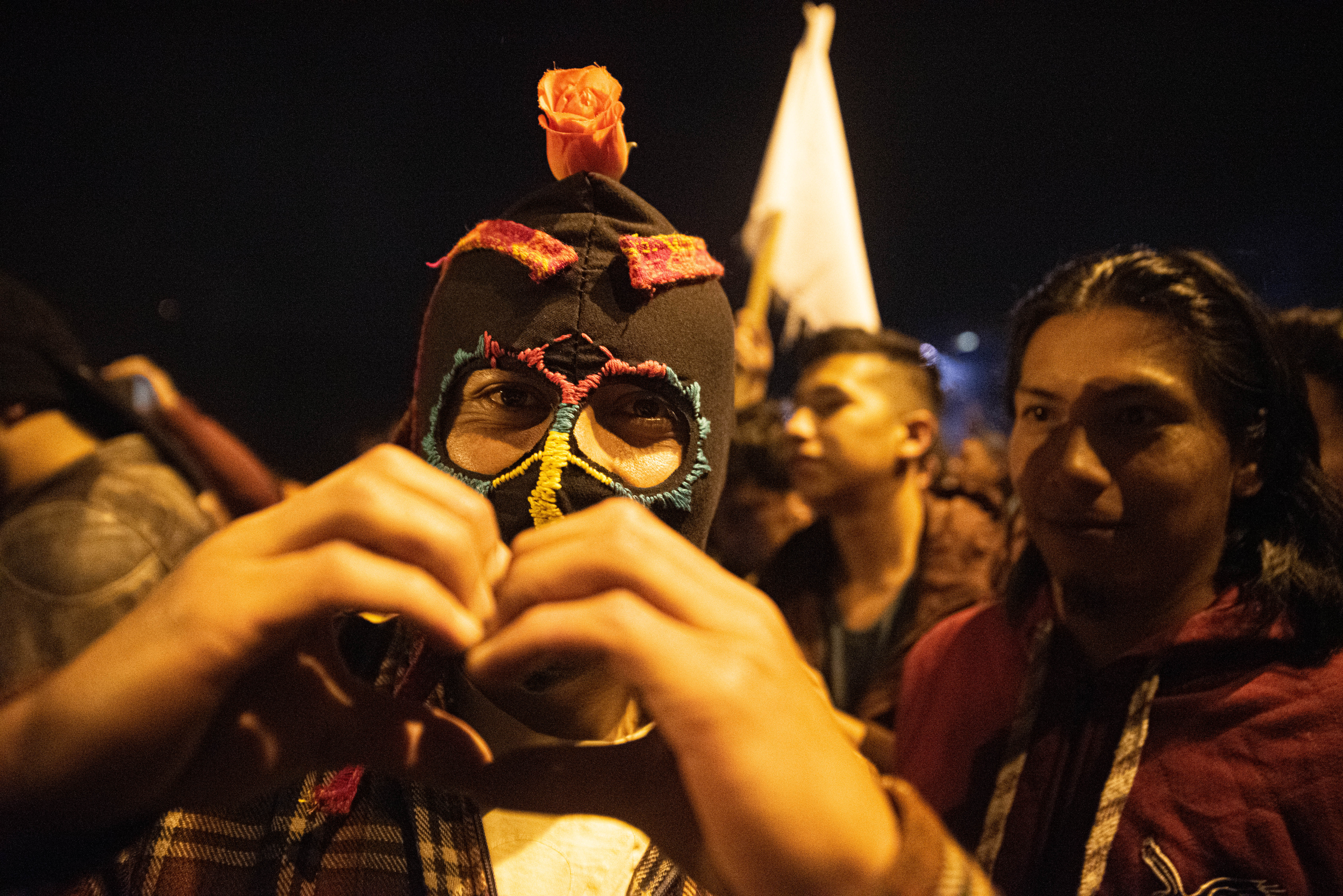 Un hombre con una mascara en los festejos del domingo por la noche hace una forma de corazón. Los manifestantes pedían