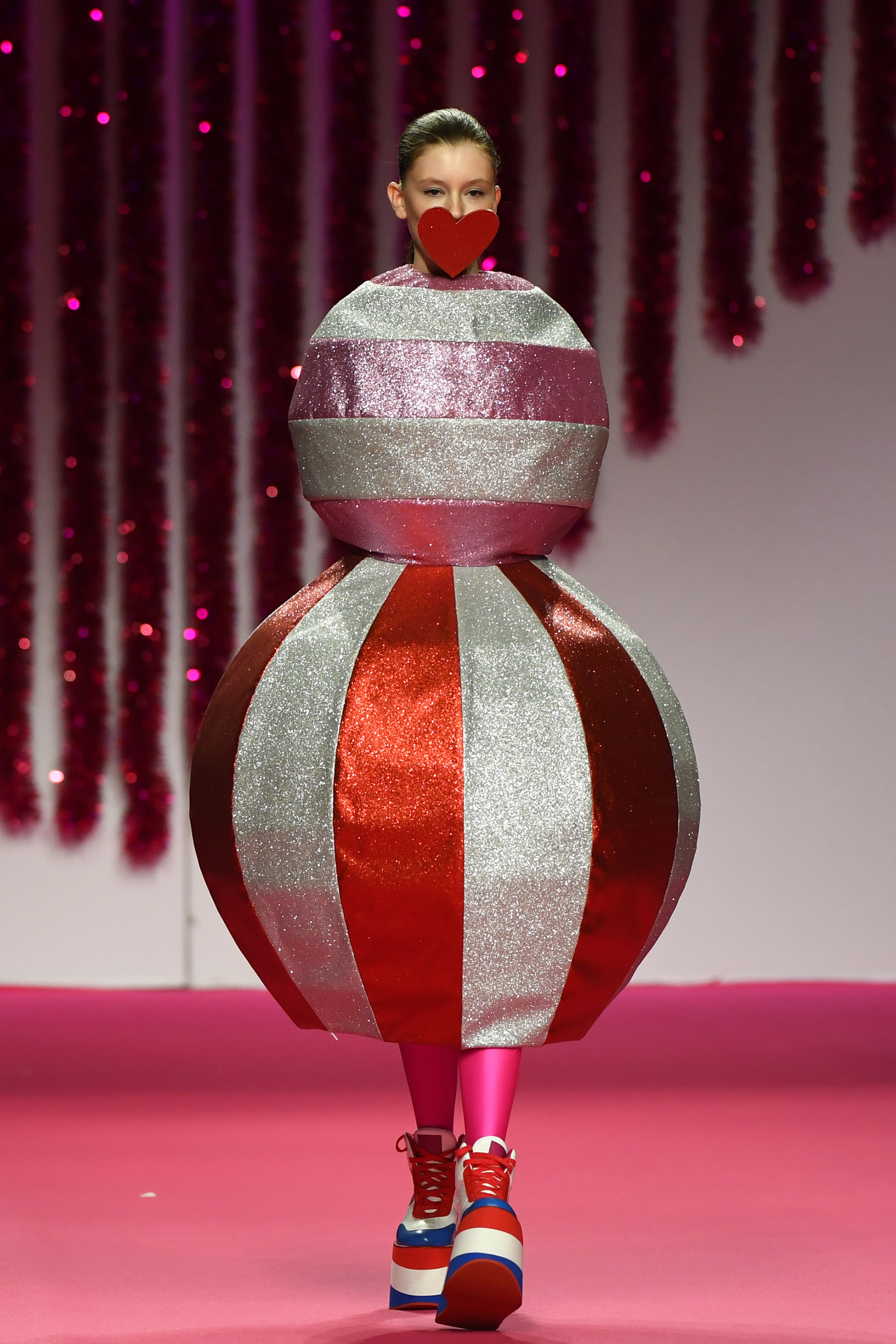 Un particular diseño de Ágatha Ruiz de la Prada: dos esferas metalizadas de glitter rayadas con mega plataformas. El estilismo del desfile consistía en tapar la boca de las modelos con corazones de cartón en rojo