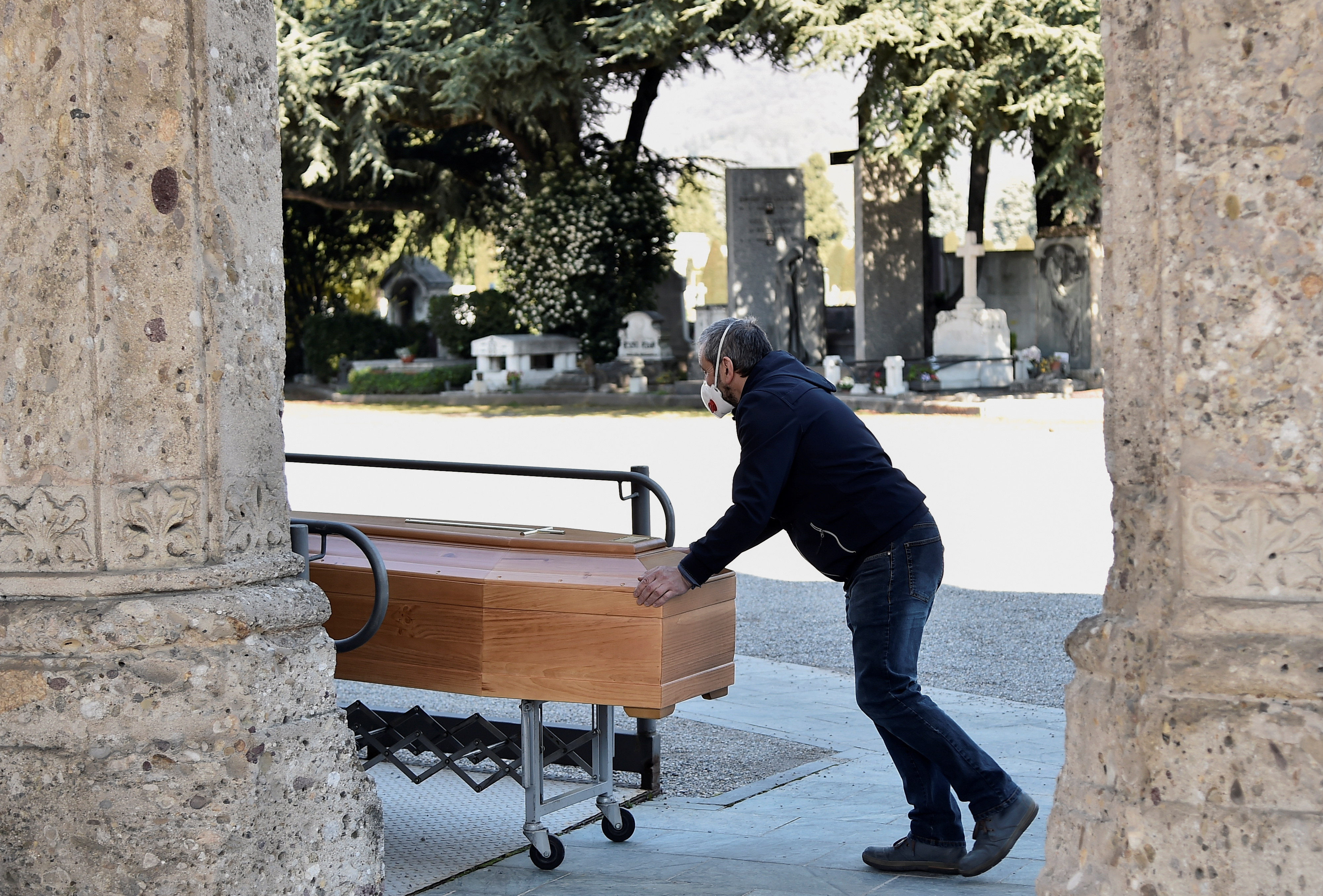 Un hombre con una máscara protectora transporta un ataúd dentro de un cementerio en Bérgamo, Italia, donde el drama es incalculable (Reuters)