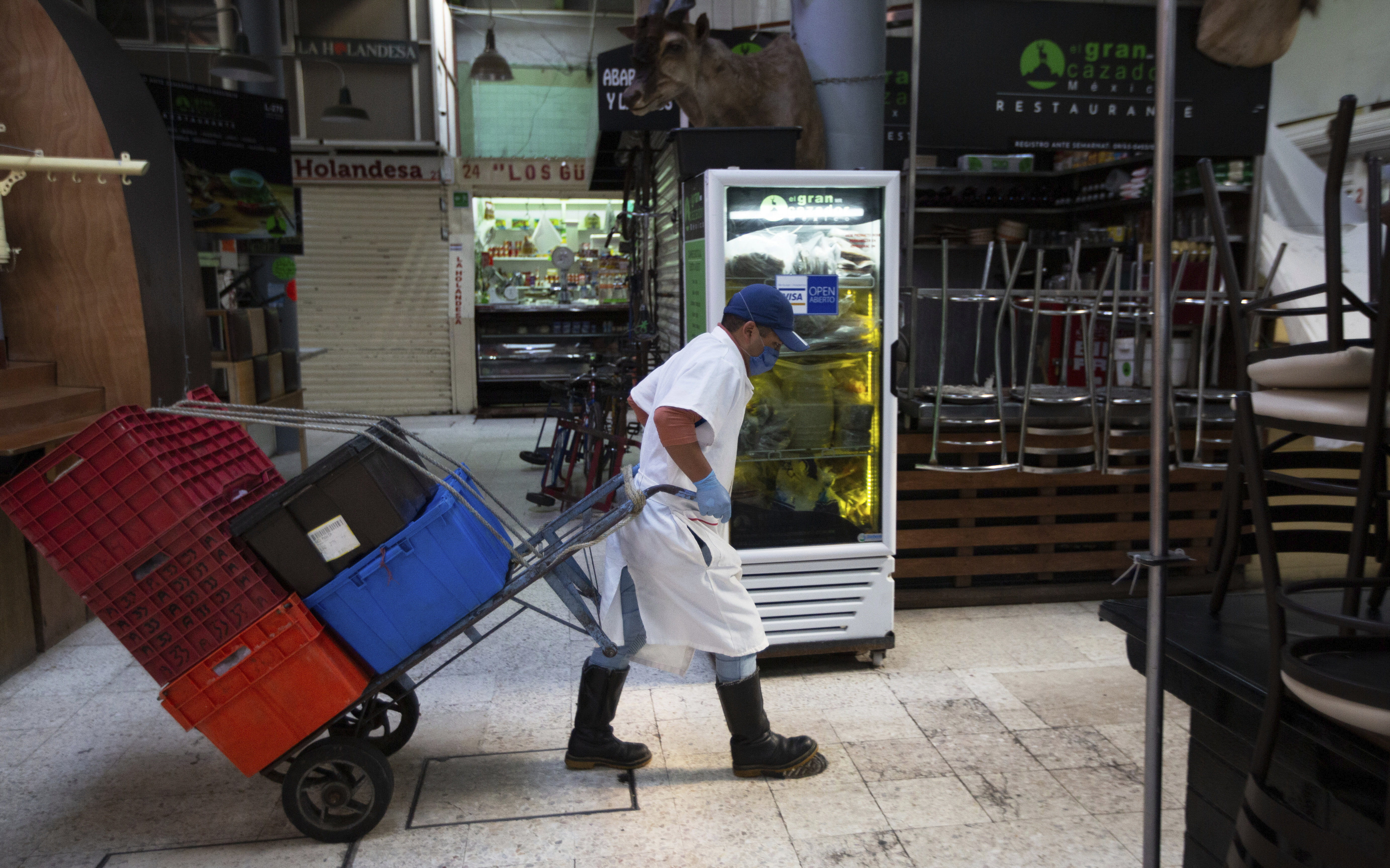 Un empleado que usa una mascarilla protectora y guantes desechables, transporta cajas con la ayuda de un carrito a través del popular y normalmente concurrido mercado de alimentos de San Juan, en la Ciudad de México, el miércoles 25 de marzo de 2020.