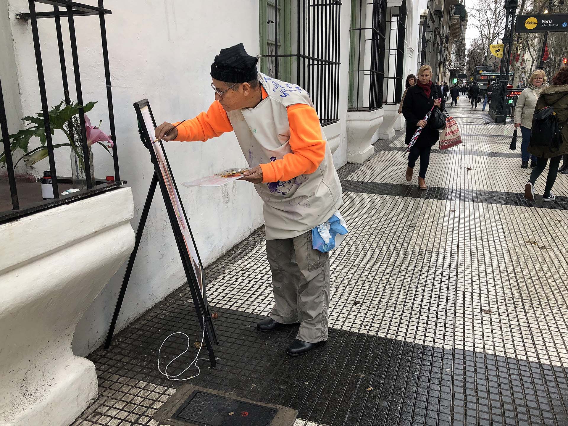 Un día de semana, minutos después de la lluvia, en Avenida de Mayo, entre Perú y la Plaza de Mayo, sobre el costado del Cabildo, un hombre se detuvo a pintar una flor en su florero.