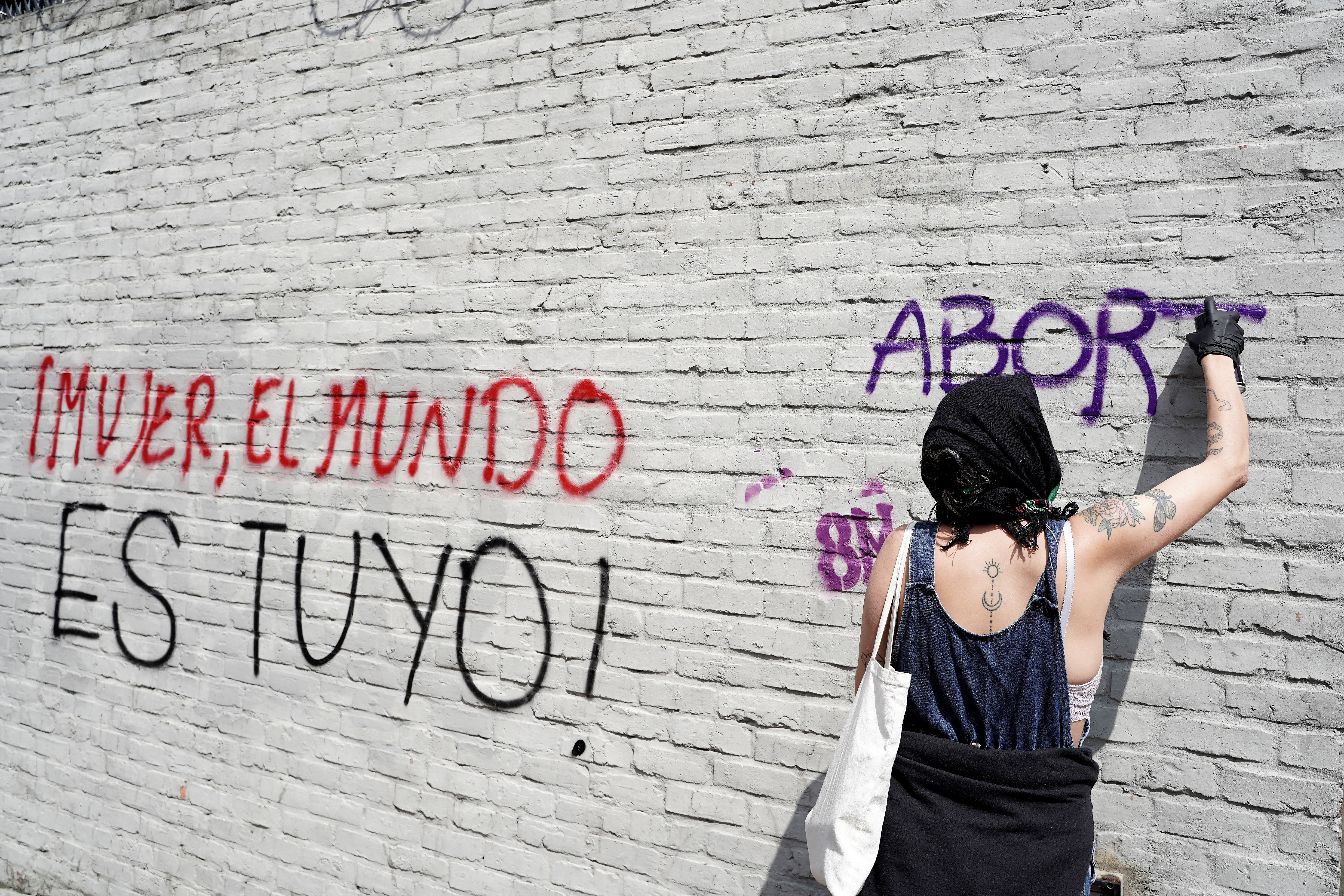 Una mujer pinta una pared con aerosol durante una marcha para conmemorar el Día Internacional de la Mujer en Bogotá, Colombia, el 8 de marzo de 2020. El graffiti dice