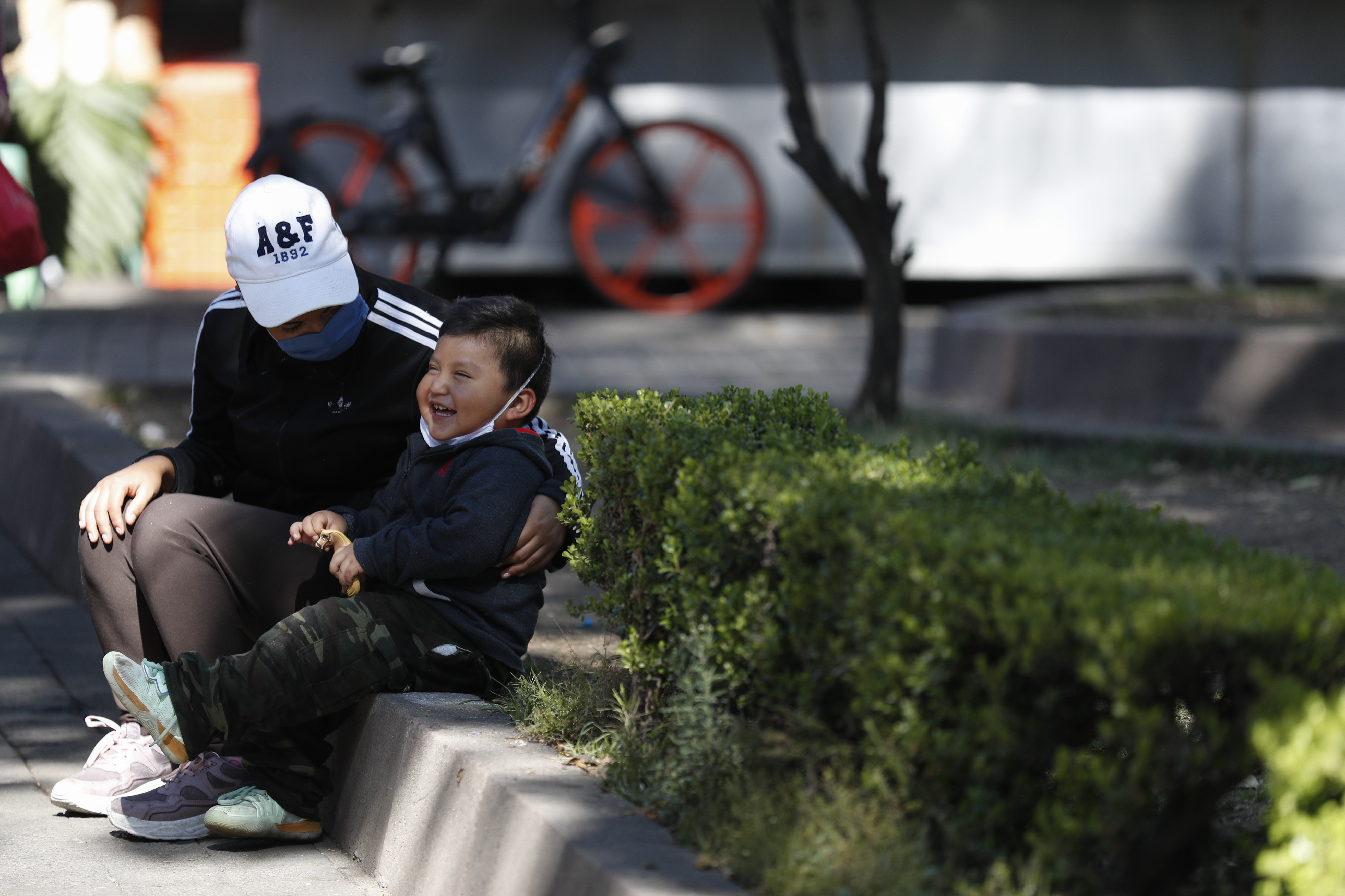 Una mujer, con una máscara facial protectora, y su hijo se sientan en una acera en la Ciudad de México, el miércoles 25 de marzo de 2020.