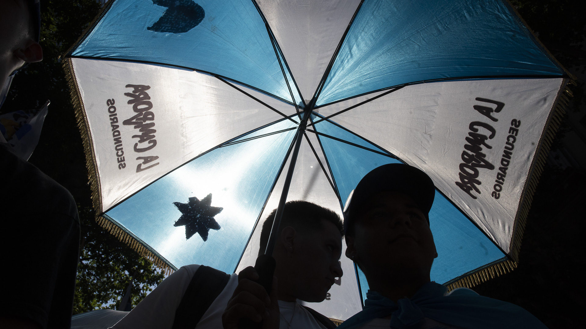 Militante de La Cámpora apovechan el paraguas de su agrupación para protegerse del intenso sol