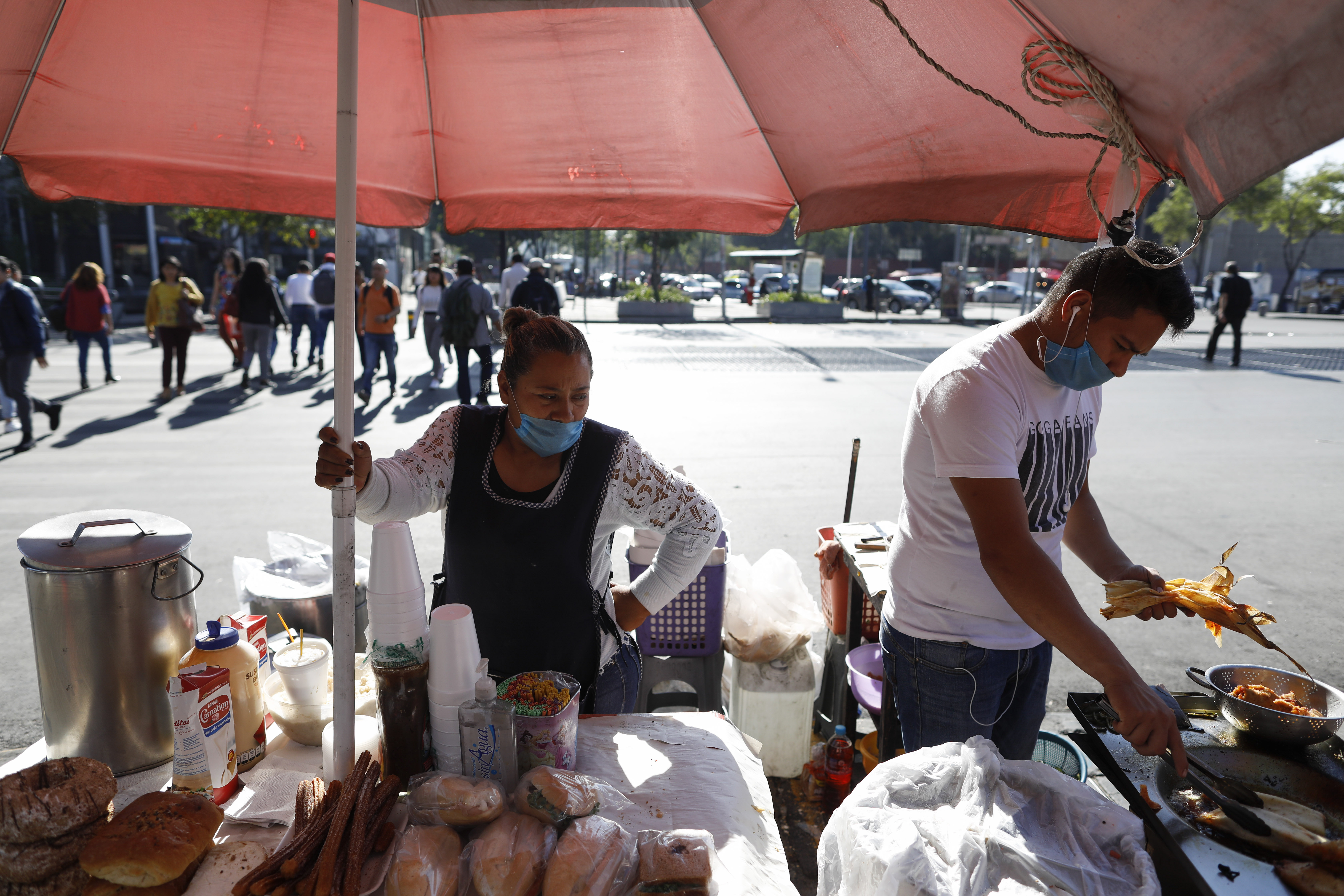 Lourdes Sanvicente, de 45 años, a la izquierda, y un compañero de trabajo usan máscaras protectoras mientras venden tamales, sándwiches y pasteles en un puesto callejero en la Ciudad de México, el miércoles 25 de marzo de 2020. Sanvicente, quien duda La existencia del nuevo coronavirus, dice que tanto ella como su esposo trabajan como vendedores ambulantes de alimentos, y juntos ganan 320 pesos (alrededor de $ 13.50) por día para mantenerse a sí mismos y a sus cinco hijos. “No hay otra opción”, dice, “tengo que mantener a mis hijos”.